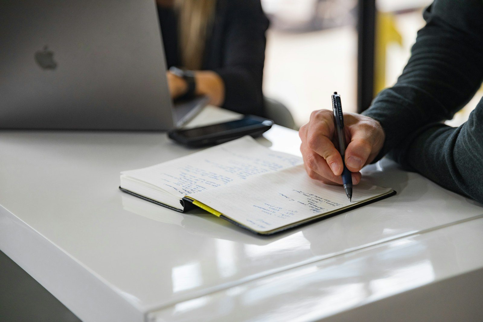 Hands writing notes beside a laptop while working through documents